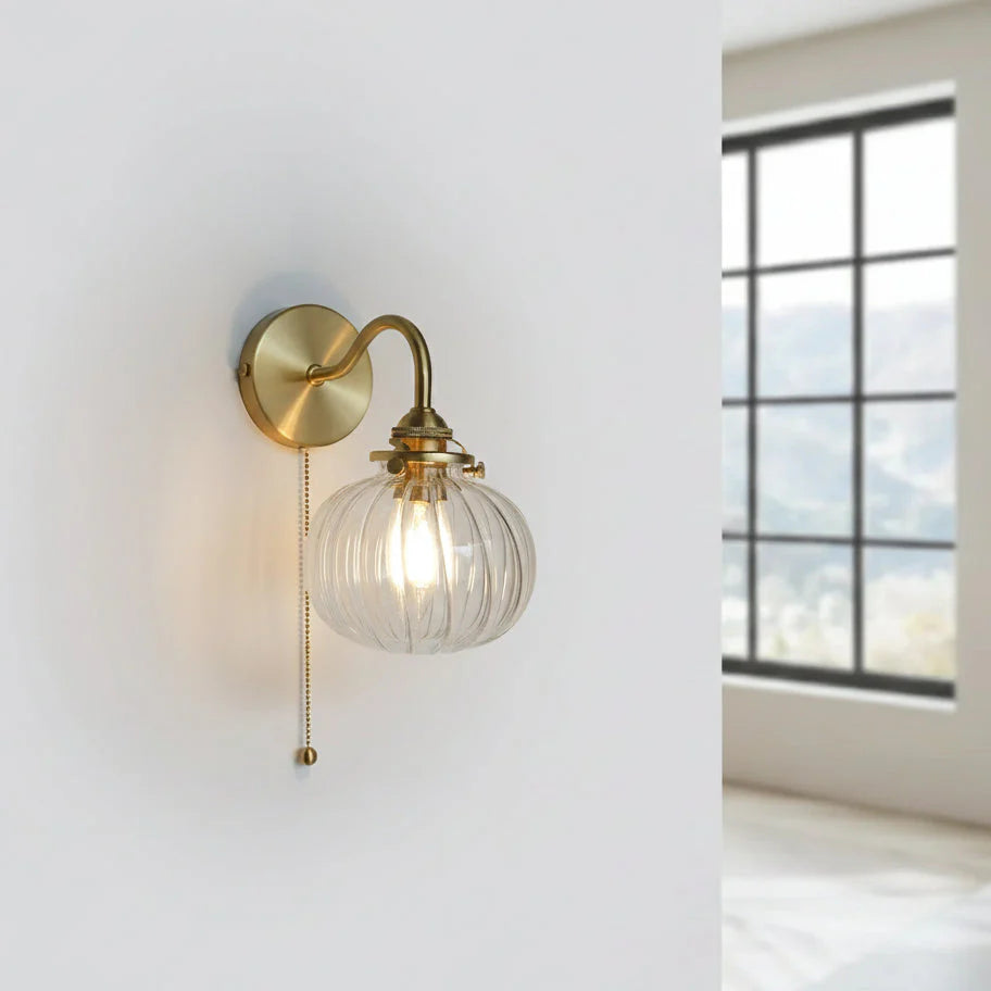 wandlamp met glazen bol en goudkleurige metalen wandplaat met trekkoord